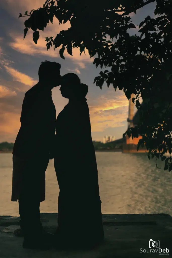 Silhouette Of Bride In Saree And Groom In Suit Standing By A River At Sunset — Romantic Pre-Wedding Portrait In Kolkata By Sourav Deb, Calcutta Wedding Photography